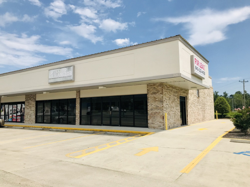 An image of a concrete building in front of a parking lot. The signs are faded and there is a signboard that says, 